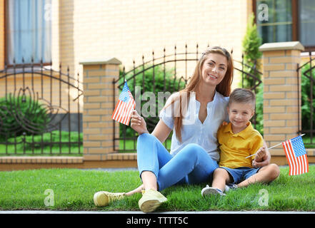 Mother and son with little American flags sitting on grass beside their house Stock Photo