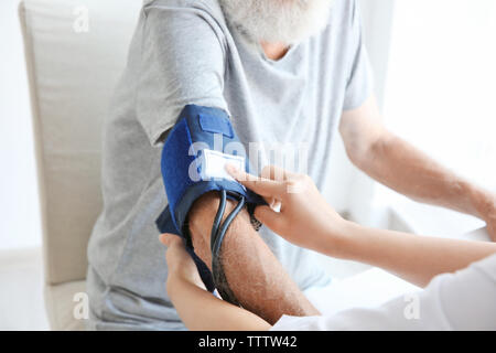 Nurse helping senior with measuring pressure at home Stock Photo