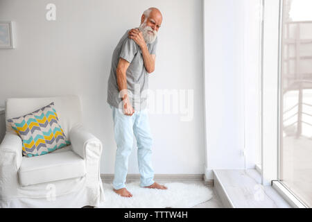 Senior man with pain in shoulder trying to stand up Stock Photo
