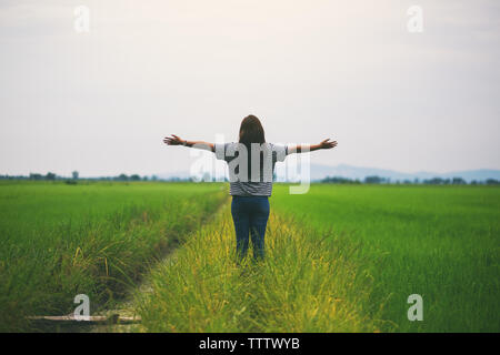 A woman standing and stretching arms in a beautiful rice field with feeling relaxed and fresh Stock Photo