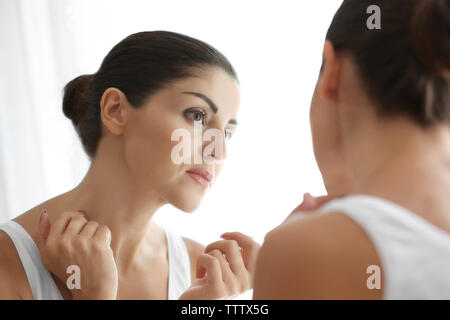 Adult woman checking her face in mirror on light background Stock Photo