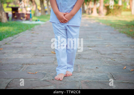 A cute Asian boy or girl walks in peace and relaxes in the garden pavilion at the temple or church and wears a white dress with sunlight on a white ba Stock Photo