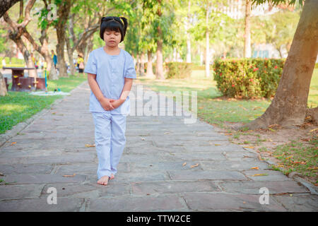 A cute Asian boy or girl walks in peace and relaxes in the garden pavilion at the temple or church and wears a white dress with sunlight on a white ba Stock Photo