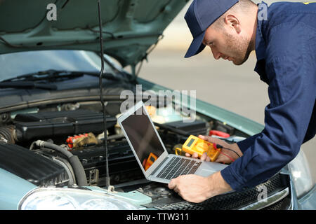 Mechanic using computer diagnostics while repairing car Stock Photo