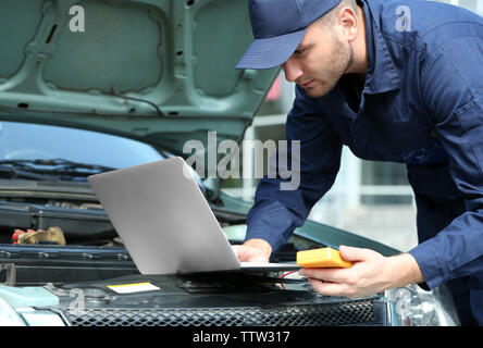 Mechanic using computer diagnostics while repairing car Stock Photo