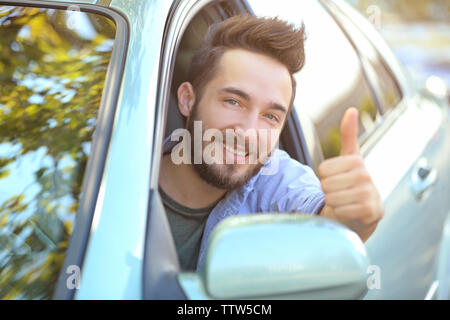 Successful young man sitting in car and showing thumb up sign Stock Photo