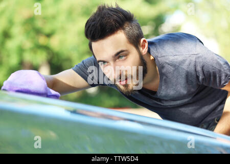 Handsome young man wiping car with special glove Stock Photo