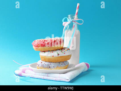 Plate with stack of delicious donuts and blurred bottle of milk on blue background Stock Photo