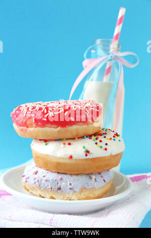 Plate with stack of delicious donuts and blurred bottle of milk on blue background Stock Photo
