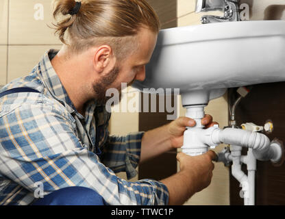 Handsome plumber assembling sink pipes in bathroom, close up view Stock Photo