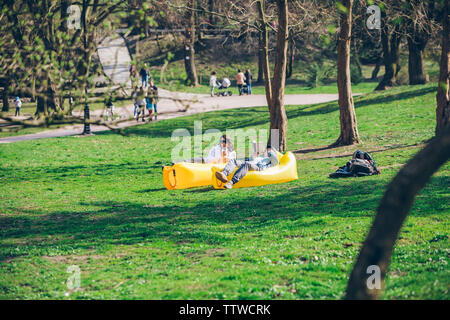 couple laying on yellow inflatable mattress in city park. reading book. drinking smoothies. leisure time Stock Photo