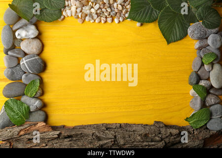 Rectangular frame made of  pebbles, leaves and bark on yellow wooden background Stock Photo