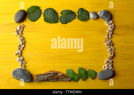 Rectangular frame made of  pebbles, leaves and bark on yellow wooden background Stock Photo