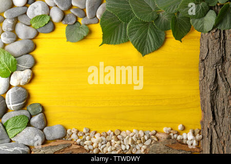 Rectangular frame made of  pebbles, leaves and bark on yellow wooden background Stock Photo