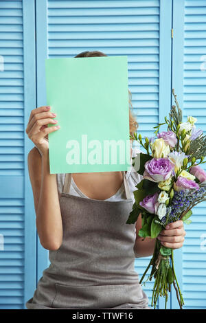 Female florist holding paper and beautiful bouquet on blue folding screen background Stock Photo