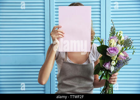 Female florist holding paper and beautiful bouquet on blue folding screen background Stock Photo