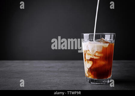 Pouring milk in iced coffee on grey background Stock Photo