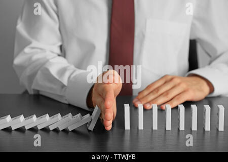 Businessman hand trying to stop toppling dominoes on table Stock Photo