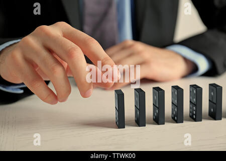 Businessman hand trying to toppling dominoes on table Stock Photo