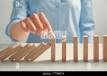 Businesswoman hand trying to stop toppling dominoes on table Stock Photo