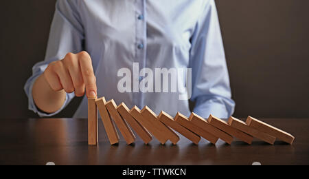Businesswoman hand trying to stop toppling dominoes on table Stock Photo