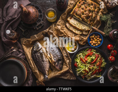 Mediterranean lunch or dinner with roasted dorado fishes, homemade focaccia bread , olive oil and olives served on rustic table with tableware and kit Stock Photo