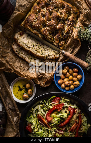 Tasty homemade focaccia bread on kitchen table background with fresh salad , olives and olive oil, top view. Italian traditional food concept Stock Photo