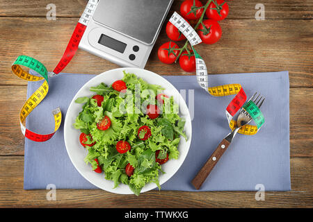 Fresh healthy salad, scales and measuring tape on wooden background Stock Photo