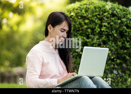Young beautiful woman working outdoor in a public park. Working on laptop outdoors. Cropped image of female working on laptop while sitting in a park. Stock Photo