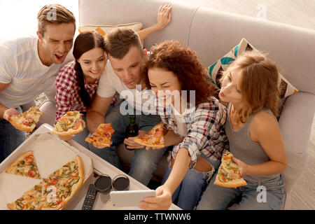 Friends taking selfie while sitting on couch and eating pizza Stock Photo