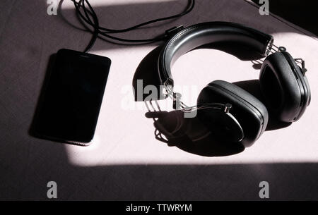 headphones and smartphone lying in the sun on a white table Stock Photo