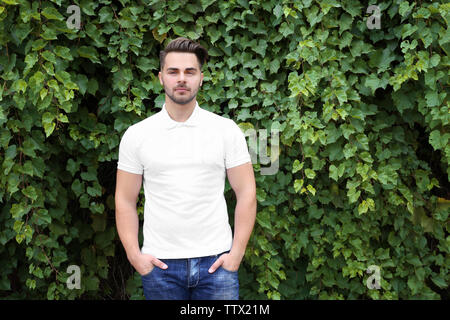 Young man in blank polo shirt on green leaves background Stock Photo