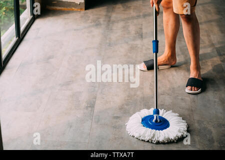 Low section of human legs and feet wearing slippers use mopping tool to clean up inside the living room at home - cleanliness and housekeeping concept Stock Photo