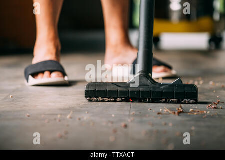 Low section of human legs wearing sandals using vacuum cleaner to hoover inside the house with dust and dirt - cleanliness and housekeeping concept Stock Photo