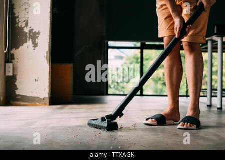 Low section of human legs wearing sandals using vacuum cleaner to hoover inside the house with dust and dirt - cleanliness and housekeeping concept Stock Photo