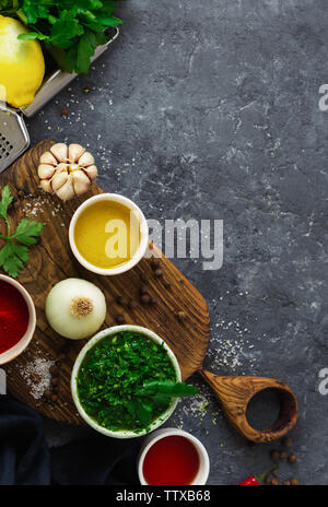 Restaurant menu concept. Ingredients for cooking Argentinian green Chimichurri or Chimmichurri salsa or sauce on dark stone background top view Stock Photo