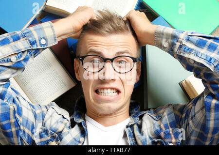 Funny young man lying on floor among books Stock Photo