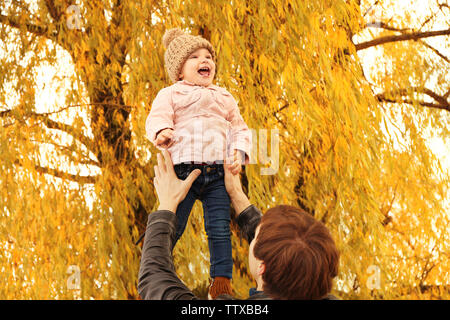 Father holding cute little girl while standing under tree in park Stock Photo