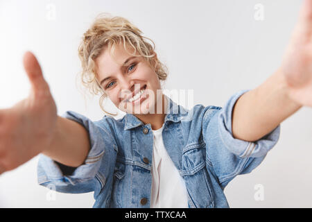 Friendly-looking happy charming blue-eyed scandinavian blond curly-haired woman tilting head smiling happily pull hands forward camera embrace you Stock Photo