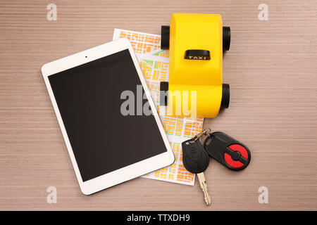 Yellow toy taxi cab, car key, tablet and map on wooden background Stock Photo