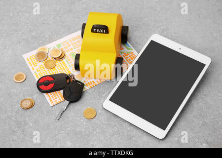 Yellow toy taxi cab, car key, tablet, coins and map on grey background Stock Photo