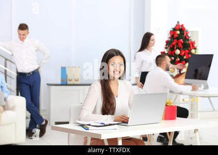 Young woman working with laptop in office decorated for Christmas Stock Photo