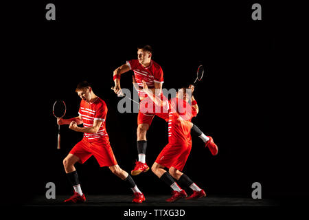 Young man playing badminton isolated on black background in mixed light. Male model in sportwear and sneakers with the racket in action, motion in game. Concept of sport, movement, healthy lifestyle. Stock Photo