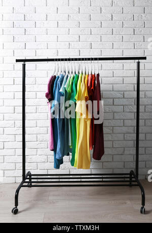 Colorful t-shirts on hangers against brick wall Stock Photo