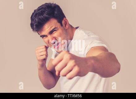 Young attractive man in rage looking furious in defence stance and threaten punching with fist in angry upset and mad face expression isolated grey ba