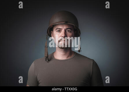 Portrait of a man in a t-shirt wearing a soldier's military helmet, staring at the camera. Stock Photo