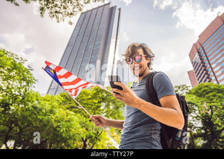 Travel and technology. Young man tourist with the flag of Malaysia is looking at a city map in a smartphone for navigation Stock Photo
