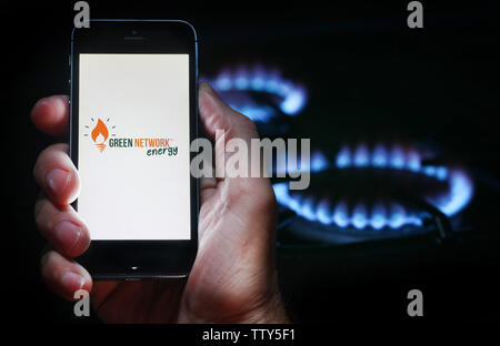 A man looking at the website logo for energy company Green Network Energy on his phone in front of his gas cooker (editorial use only) Stock Photo