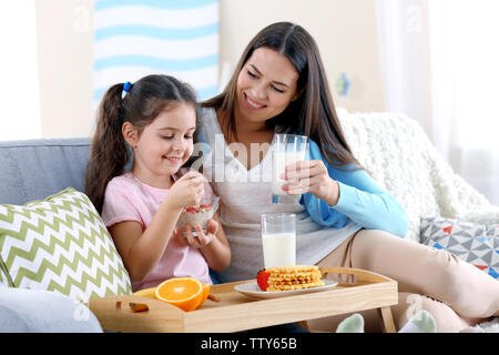 Mother and daughter having healthy breakfast on sofa in room Stock Photo