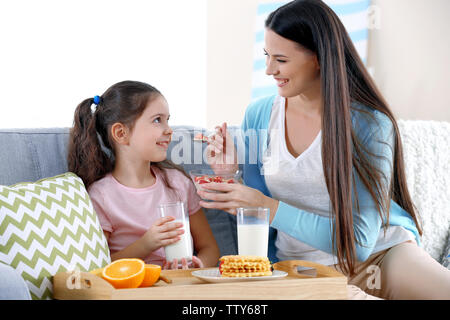 Mother and daughter having healthy breakfast on sofa in room Stock Photo